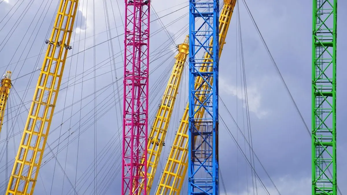 Brightly colored construction cranes rise against a cloudy sky in Greater London.
