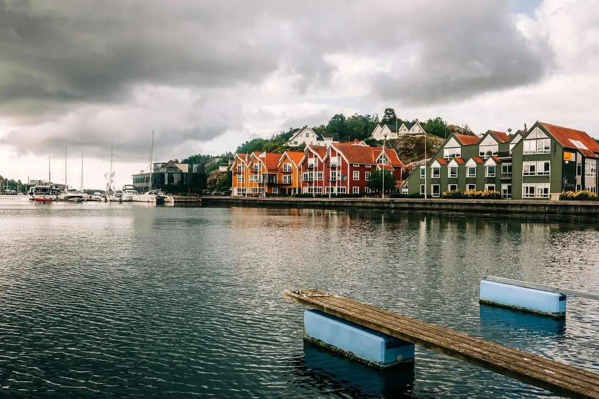 Picturesque Norwegian waterfront town with colorful homes and moody sky reflections.