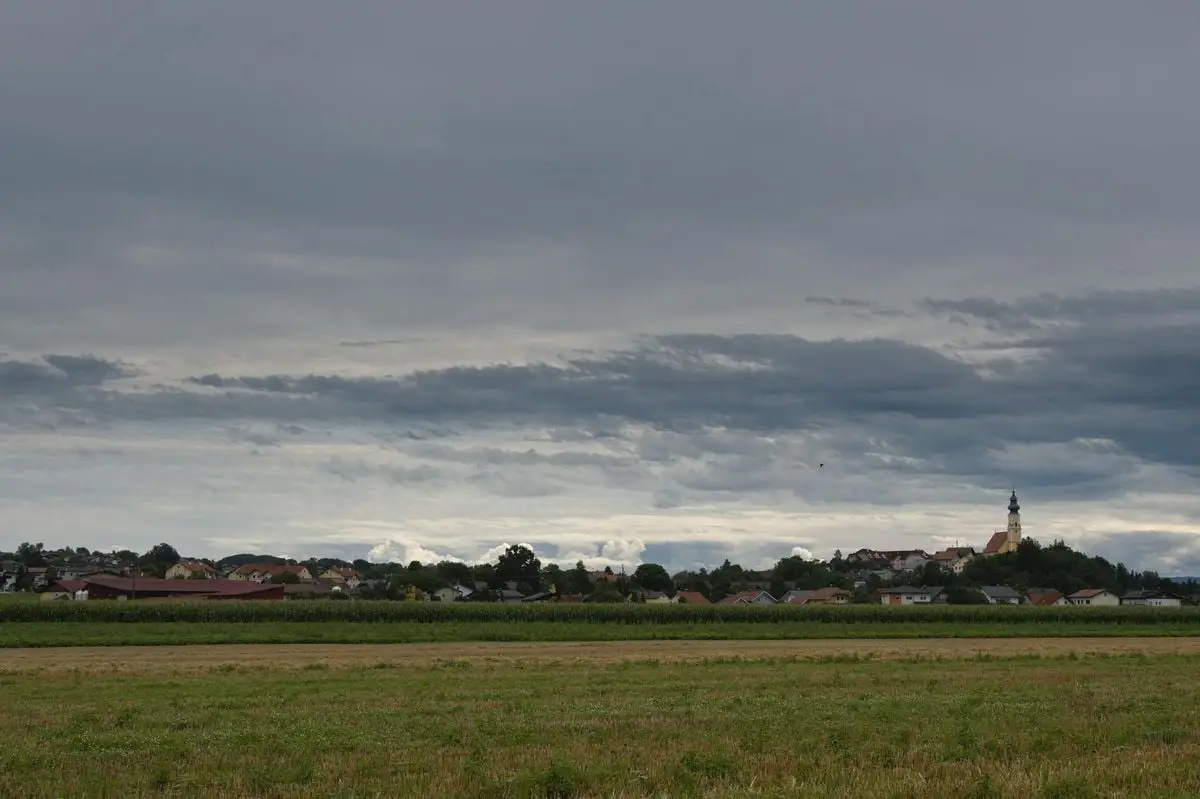 Panoramic view of a rural village in Austria with a bell tower and cropland.