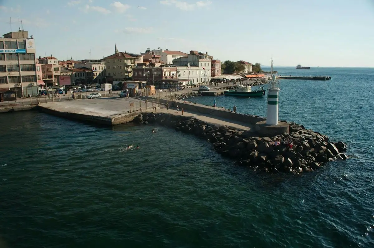 A picturesque view of Çanakkale harbor with a lighthouse and city buildings in the background.