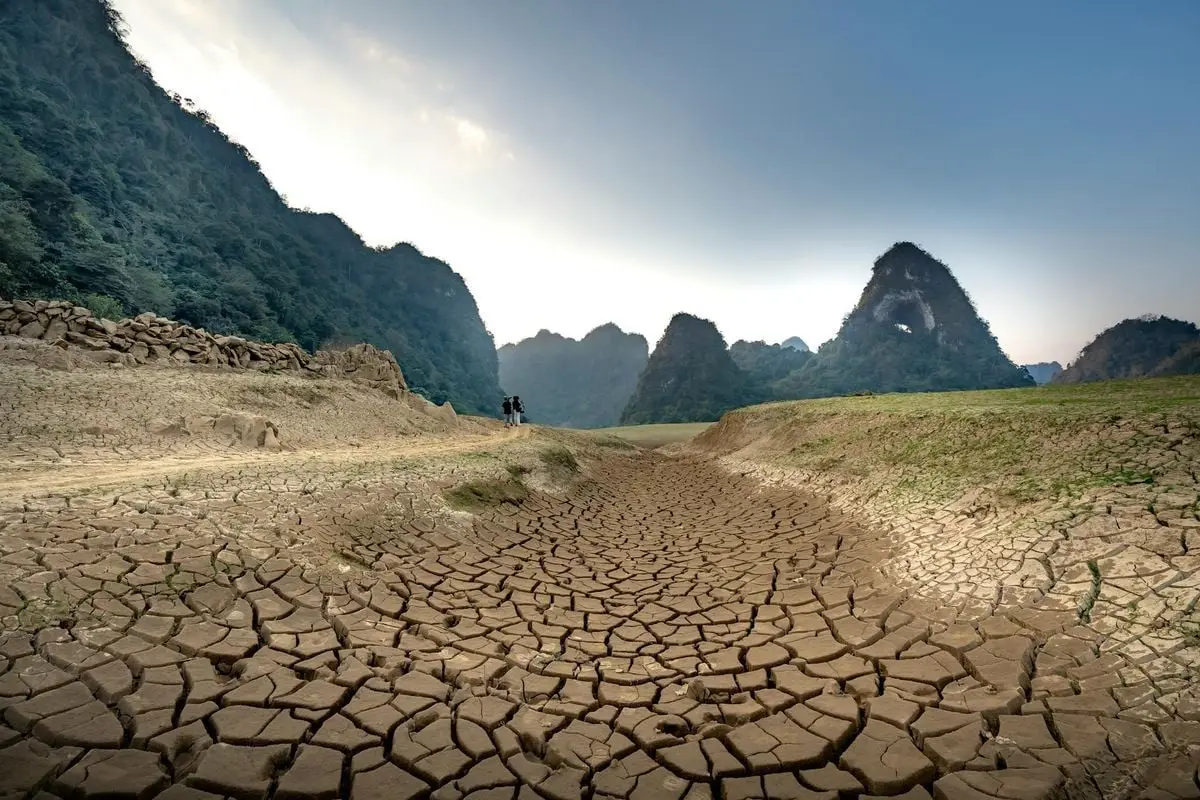 A wide shot of cracked earth with lush mountain backdrop, highlighting drought