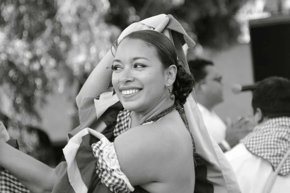Smiling woman enjoying a traditional dance outdoors. Black and white photo captures cultural celebration.