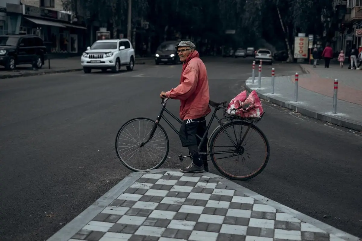 Man with bicycle stops at urban intersection on a cloudy day, showcasing city life.