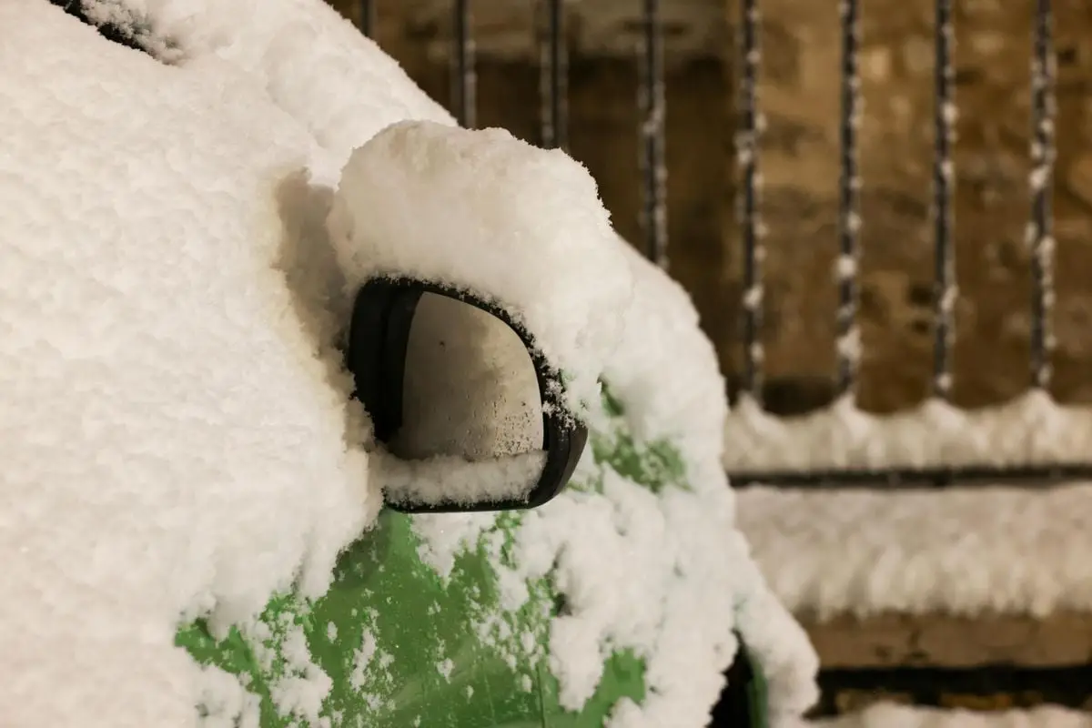 Close-up of a snow-covered green car mirror during wintertime, highlighting cold weather.