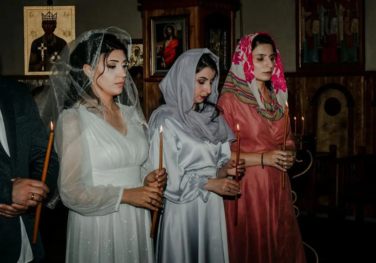 Women dressed in traditional garments holding candles during a religious service in a church.