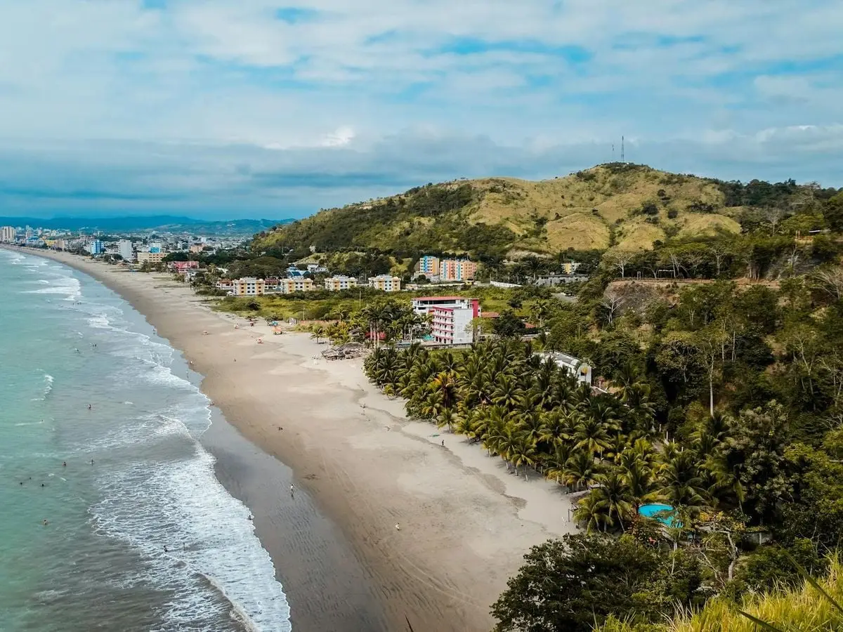 Scenic aerial view of a coastal town with tropical beach and lush hills.