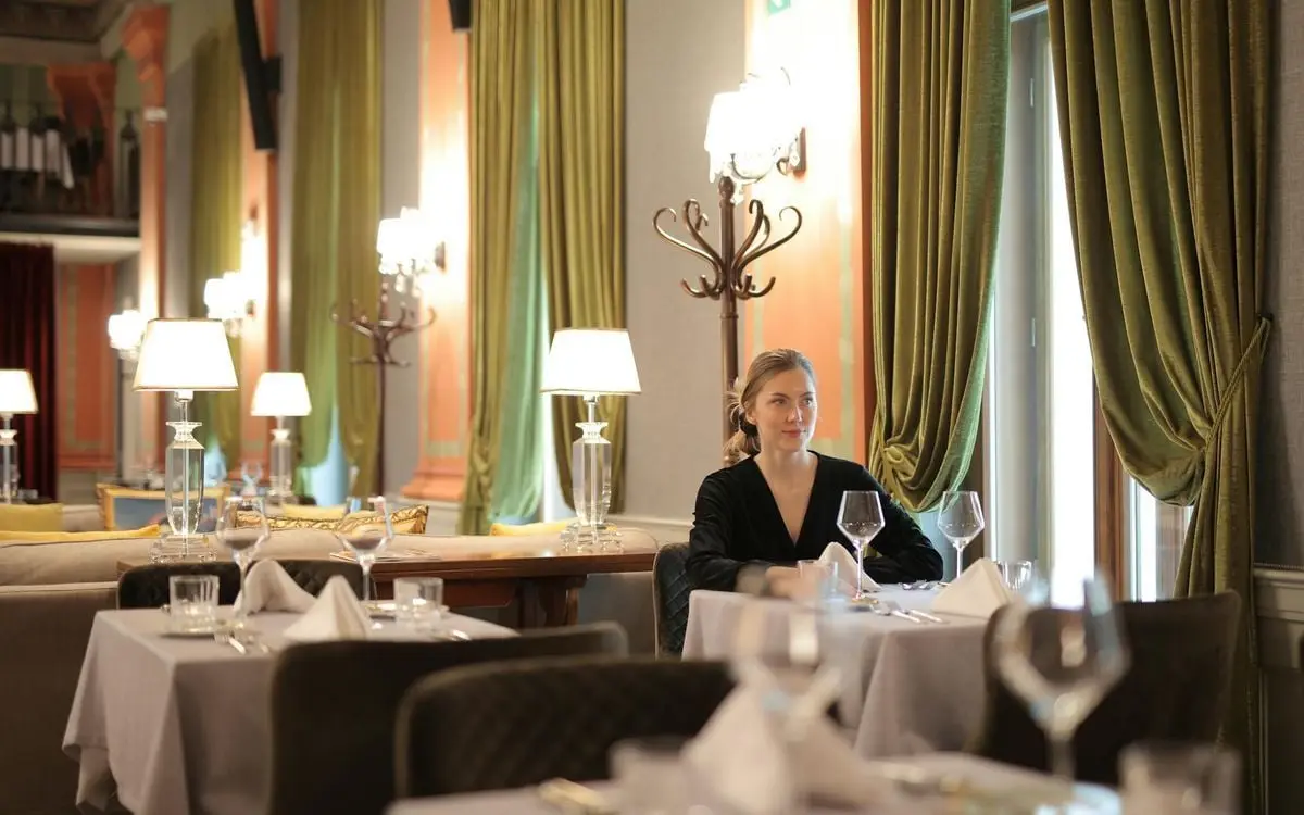 A woman seated alone at a beautifully set table in an upscale restaurant with elegant decor.