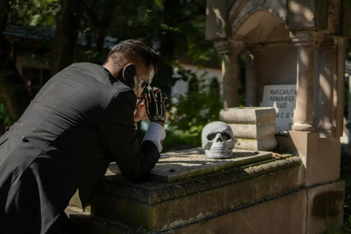Day of the Dead scene with a man in Catrin makeup by a tomb in Mexico City.