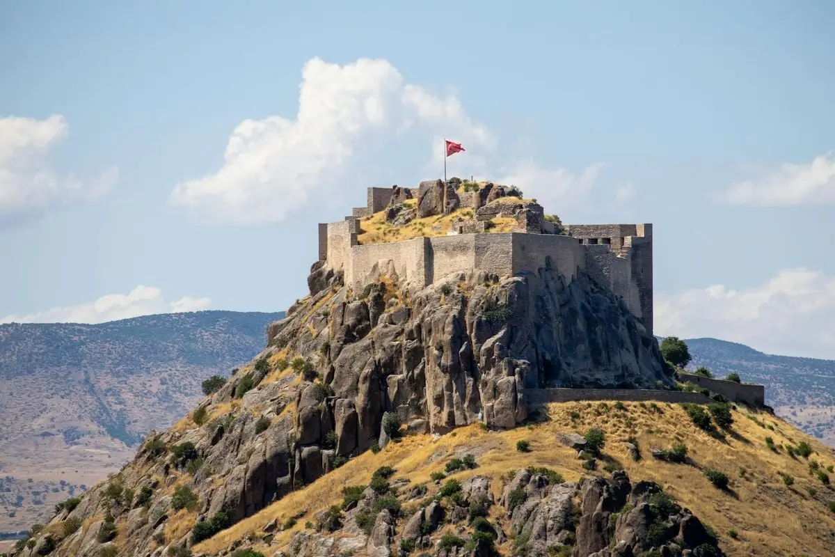 A captivating view of the ancient Pertek Castle atop a rugged hill, under a clear blue sky.