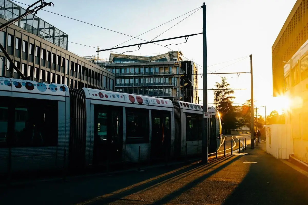 Tram riding on railroad on city street in summer in evening time near buildings