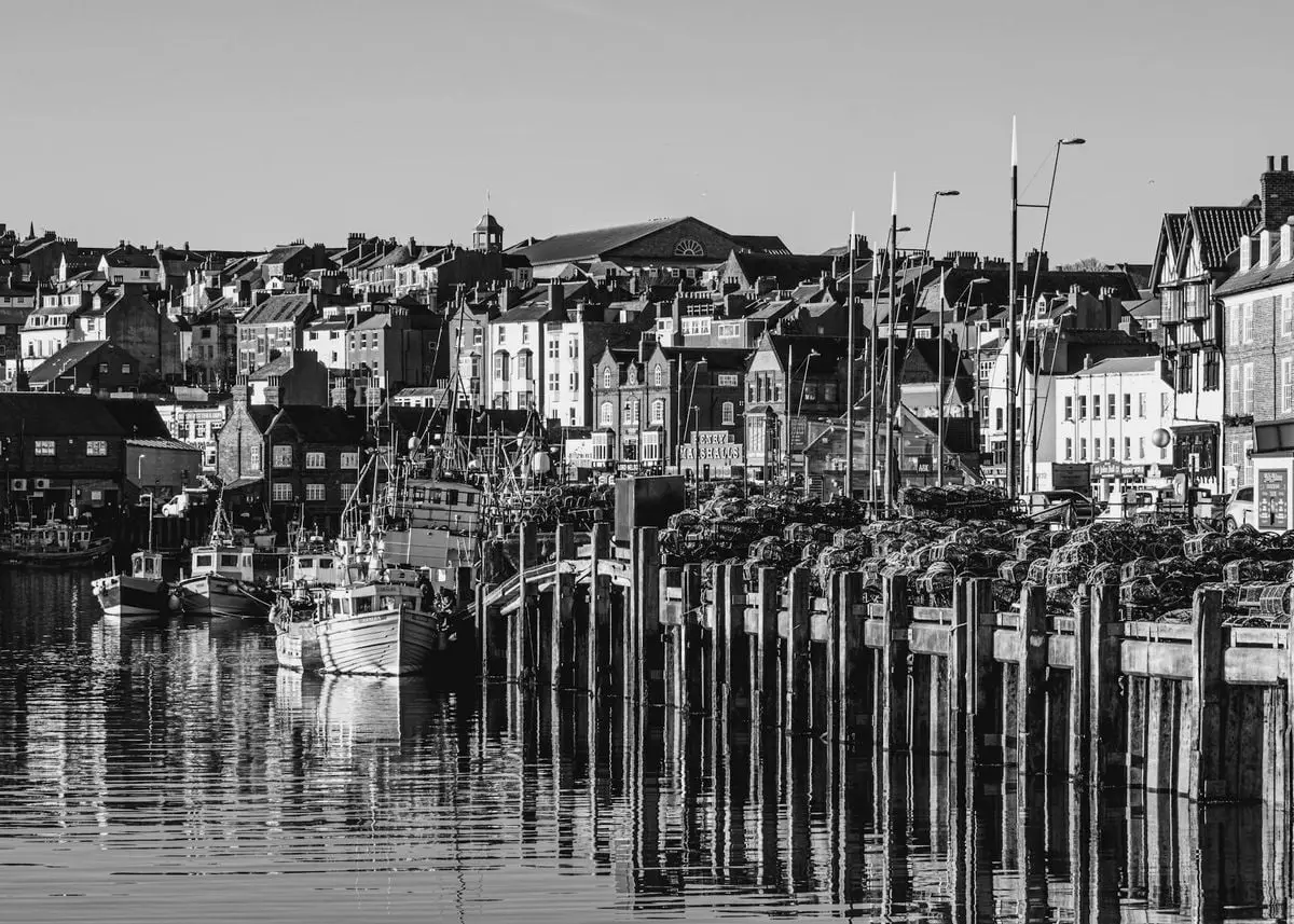 Monochrome cityscape of Scarborough harbor with fishing boats and historic buildings.