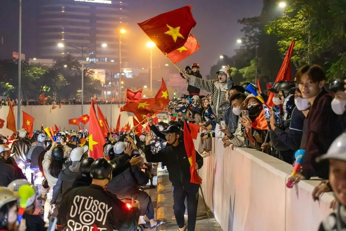 Crowd celebrating on Hanoi streets at night with Vietnamese flags and a festive atmosphere.