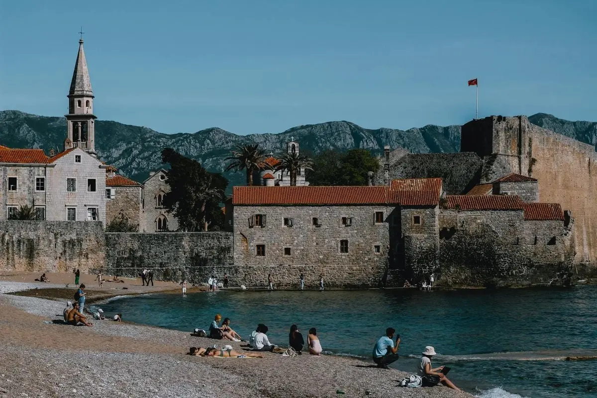Sunny day at Budva Beach featuring the historic medieval town walls and mountains.