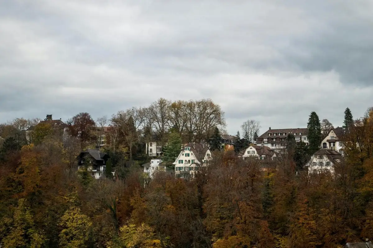 Scenic autumn view of a quaint village in Thun, Switzerland surrounded by vibrant fall foliage.