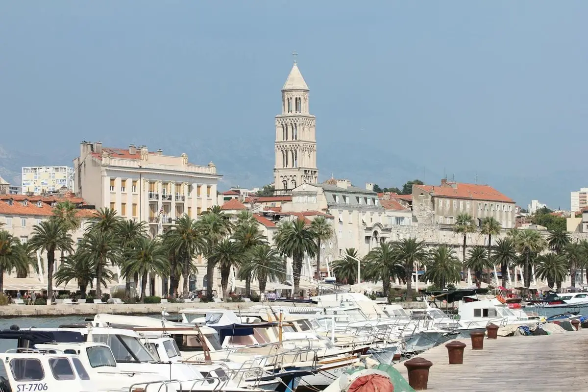 Sunlit view of Split marina with palm trees, boats, and historic buildings in Croatia.