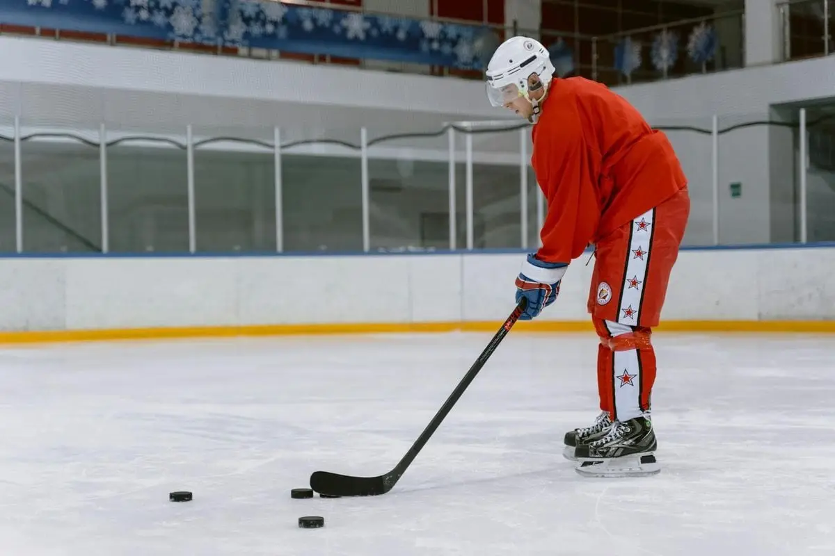 A male ice hockey player practicing on an indoor ice rink with a hockey stick and pucks.