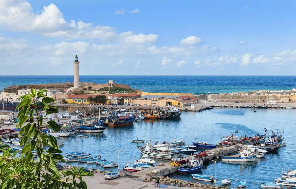 Beautiful harbor scene with various boats, lighthouse, and clear blue skies.