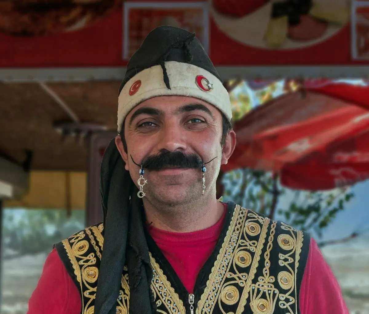 Turkish ice cream vendor smiling while dressed in traditional attire with a decorative hat.