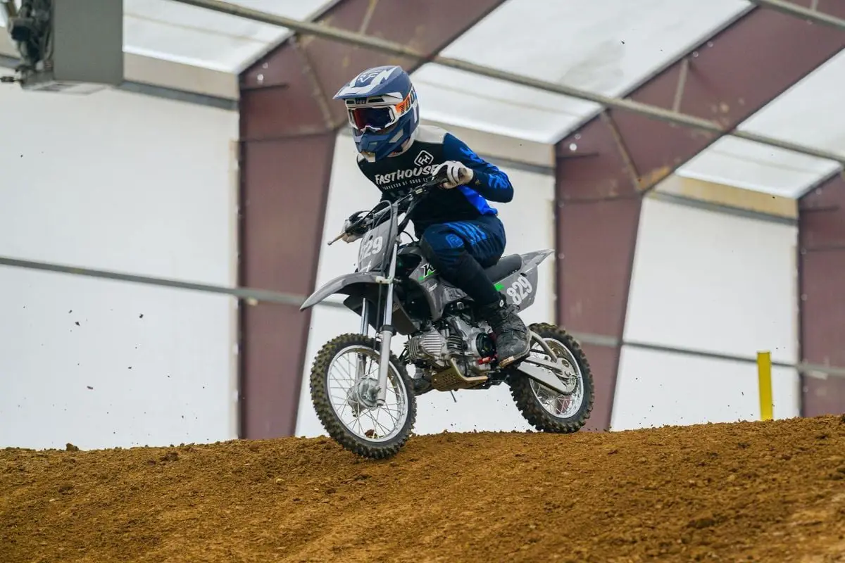 Thrilling motocross action with rider performing in an indoor arena, showcasing skill and dirt track speed.