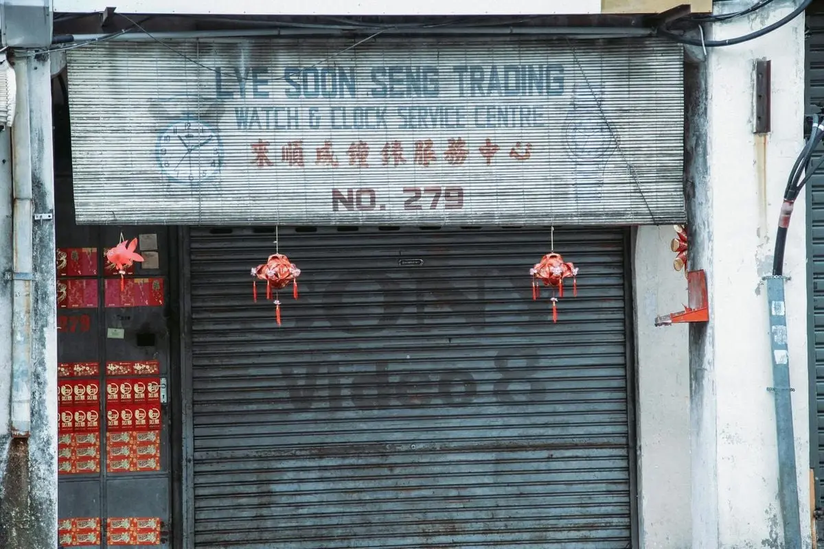 Exterior of closed aged service with signboard and traditional hanging decorations and black rolling gates located on street in city