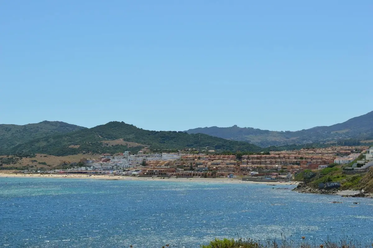 Panoramic view of a coastal town by the sea with mountains in the background.