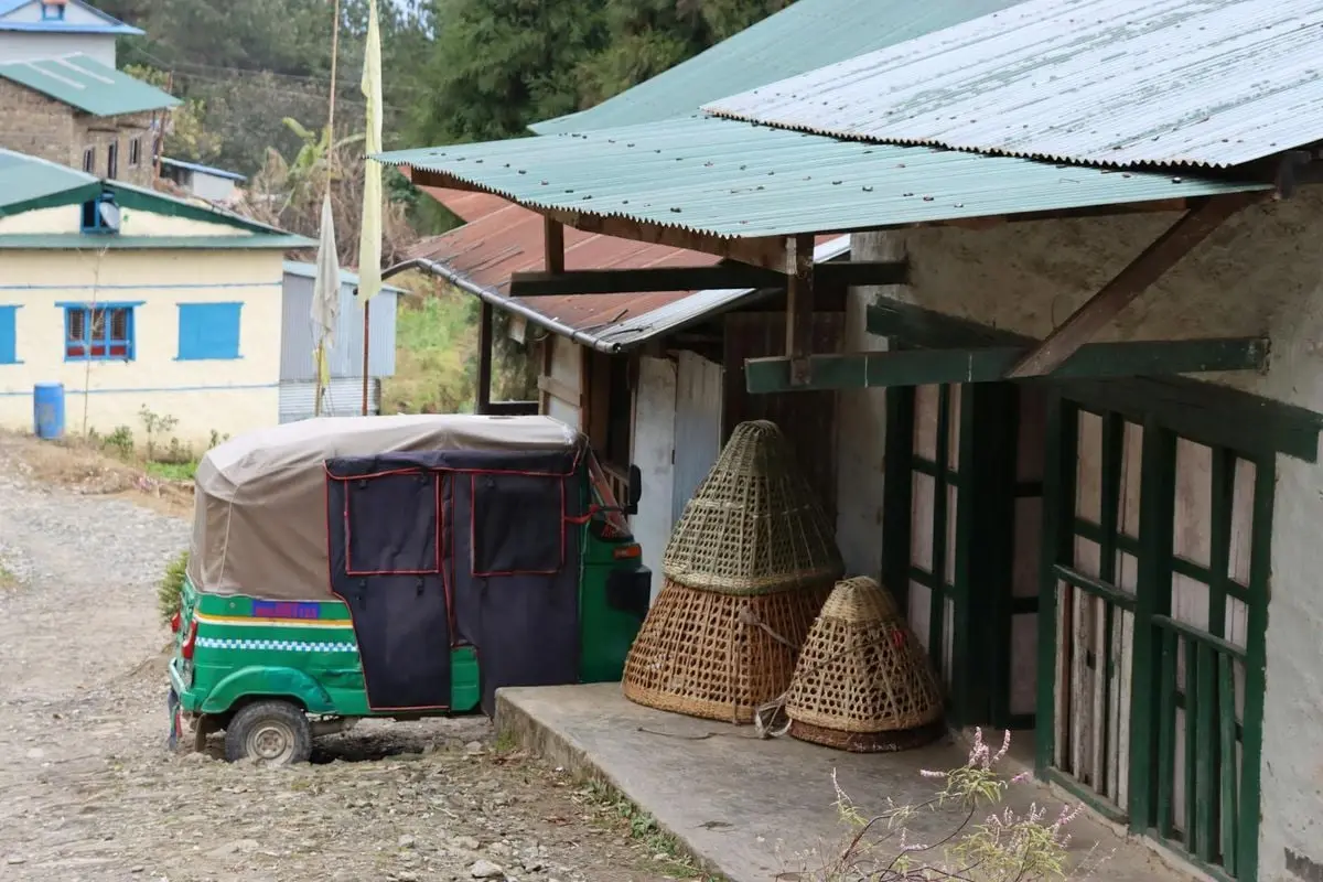 A serene rural street scene featuring a parked rickshaw and traditional wicker baskets outside rustic buildings.