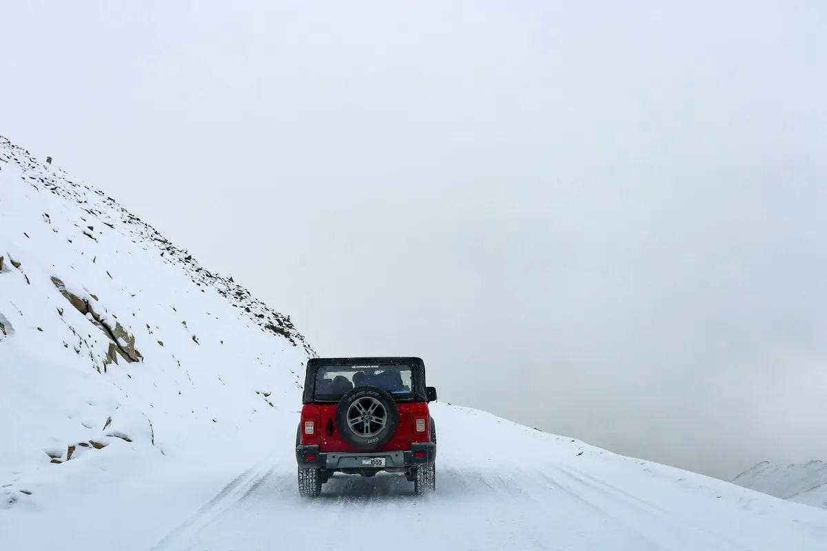 A red SUV travels along a snowy mountain road in Leh, showcasing winter adventure on challenging terrain.