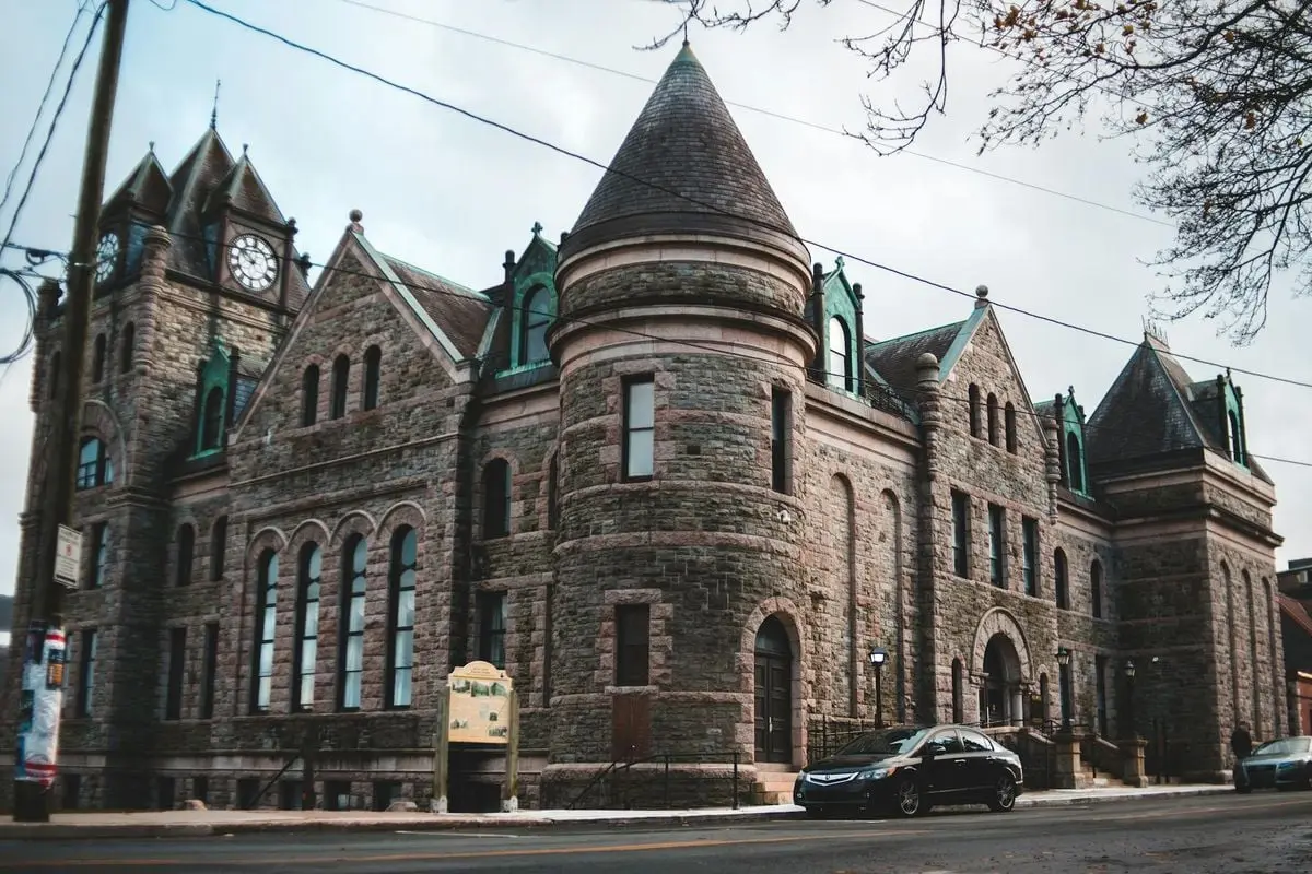 A grand historic stone building with a clock tower, set in daylight with cars parked nearby on the street.