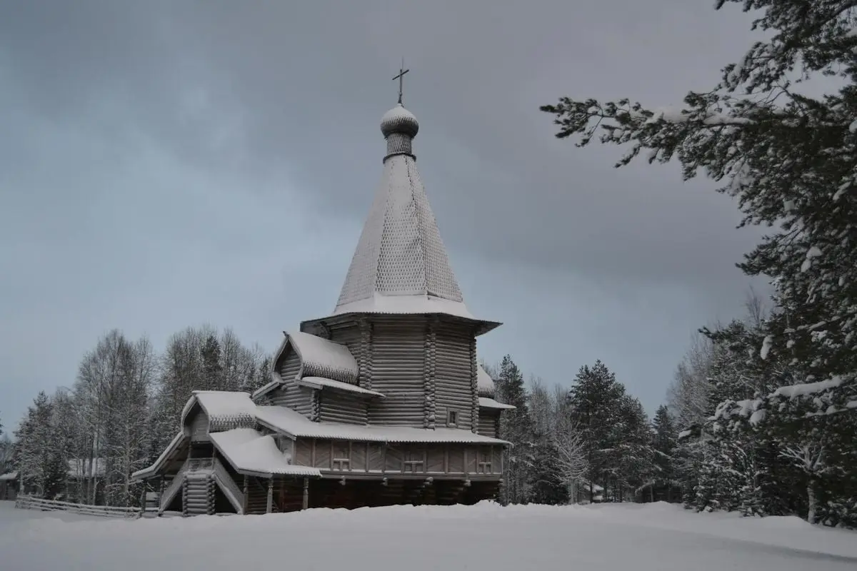 Snow-covered wooden church in a serene winter landscape in Malye Korely, Russia.