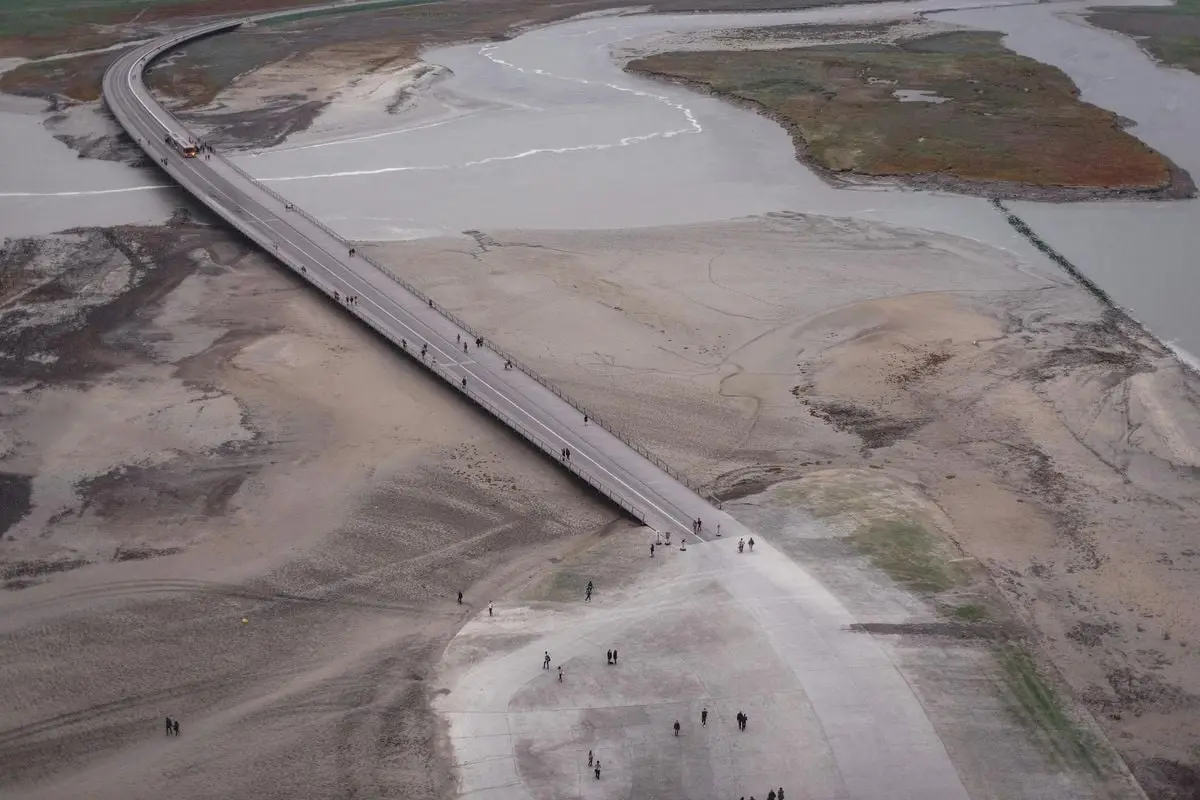 Aerial shot showing a bridge crossing over a barren landscape, sparse vegetation.