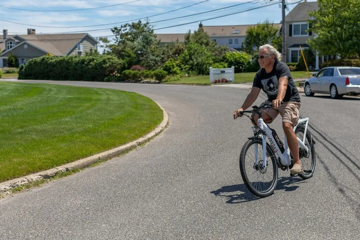 A man enjoying a ride on an electric bicycle in a sunny suburban street in Patchogue, NY.