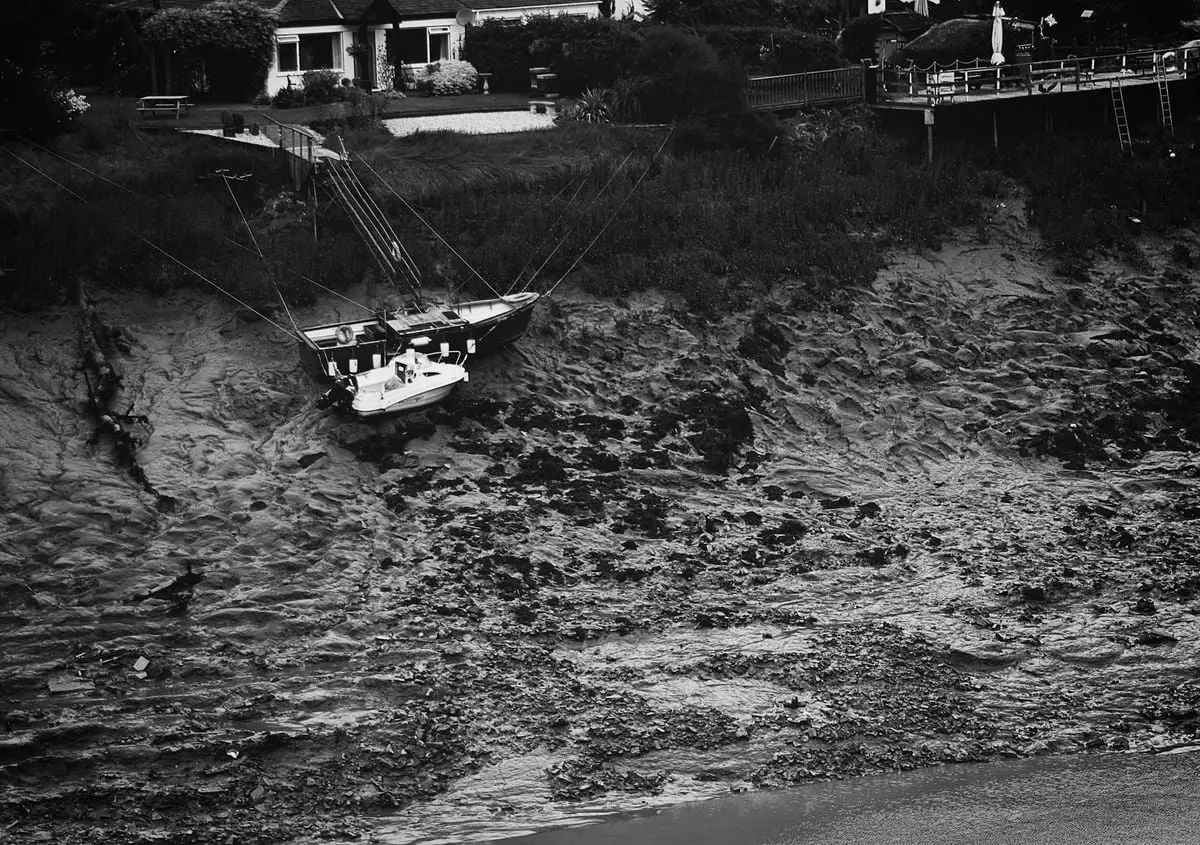 Black and white photo of boats stranded on a mud cliff near cottages in Ceredigion, Wales.
