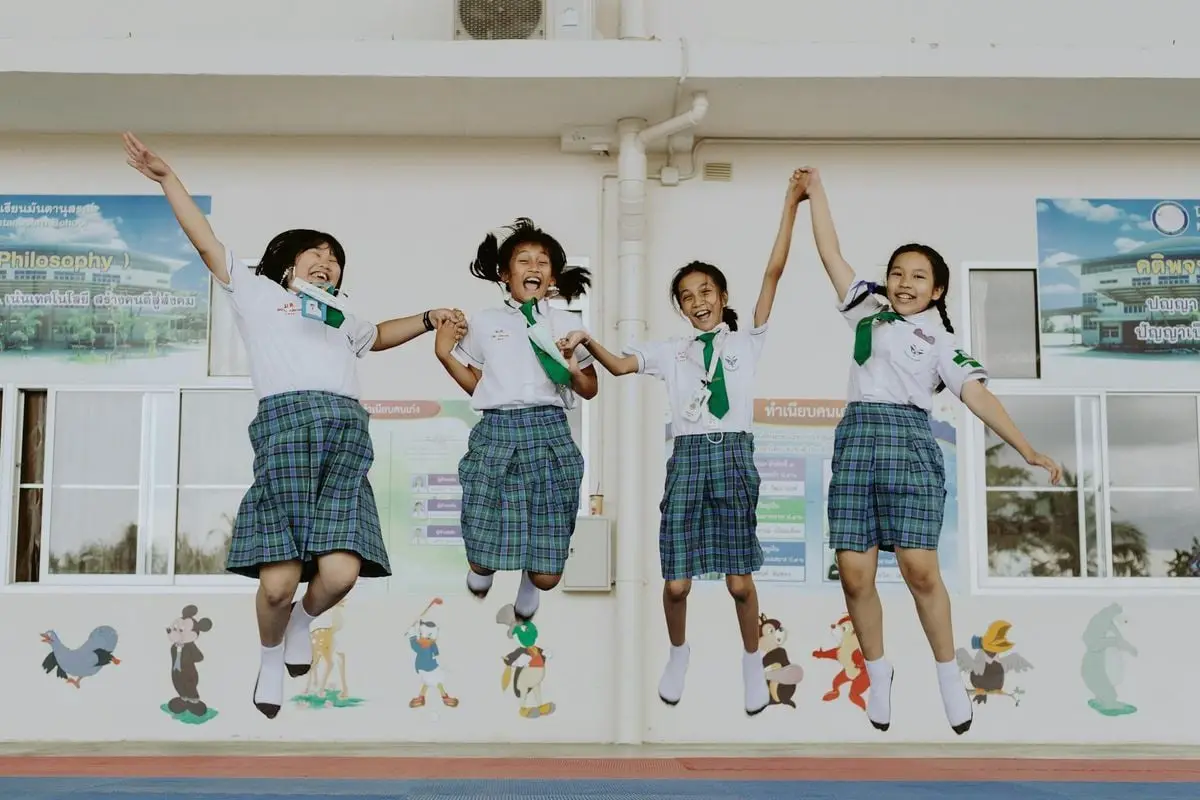 Four Asian schoolgirls jumping joyfully in uniforms at a school setting.
