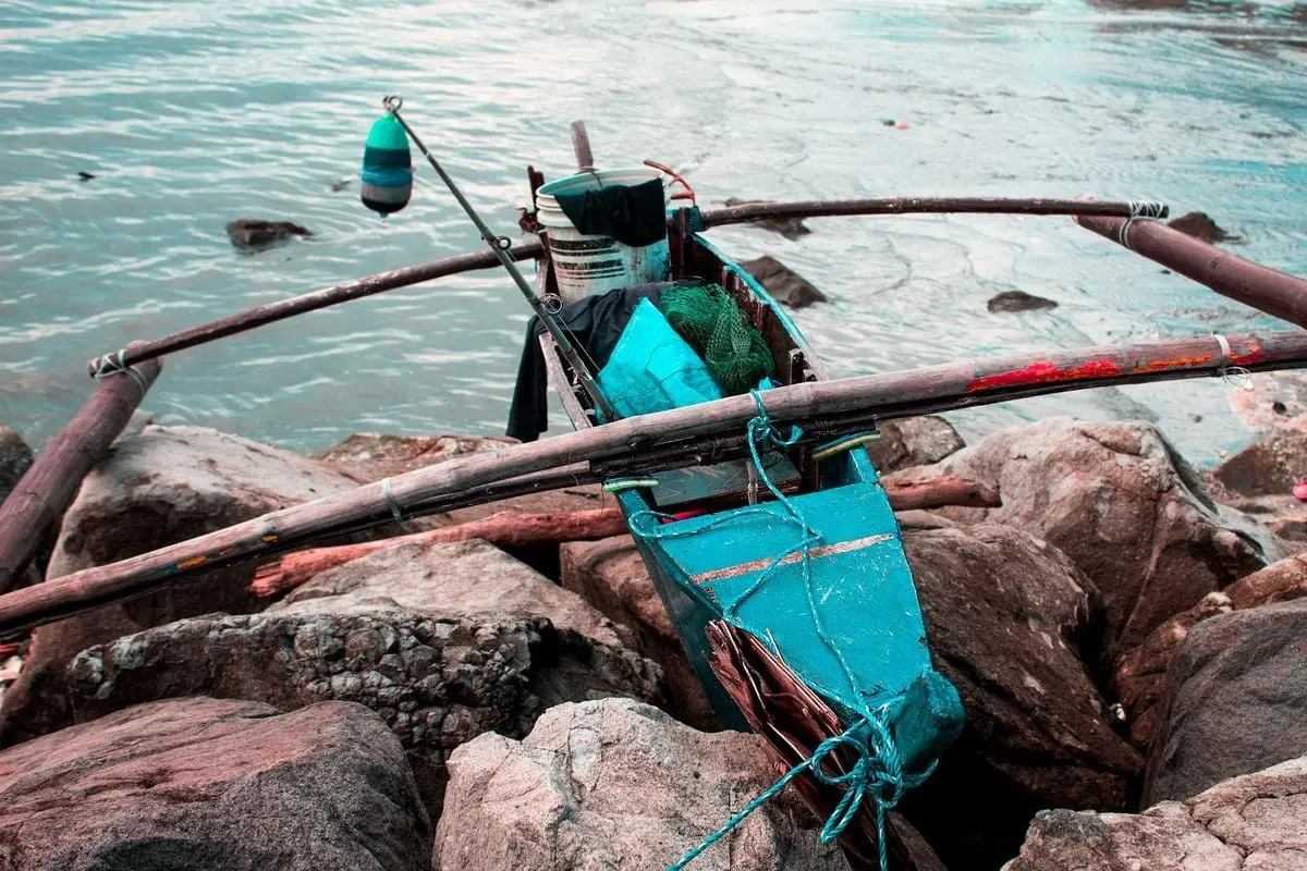 Colorful fishing boat docked on rocky seashore with ropes and nets, ready for adventure.