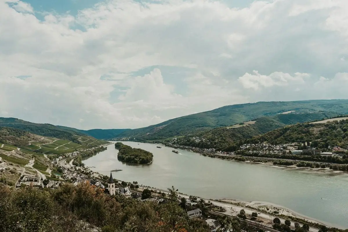 Aerial view of the Rhine River winding through the picturesque town of Rüdesheim in Germany, surrounded by hills.