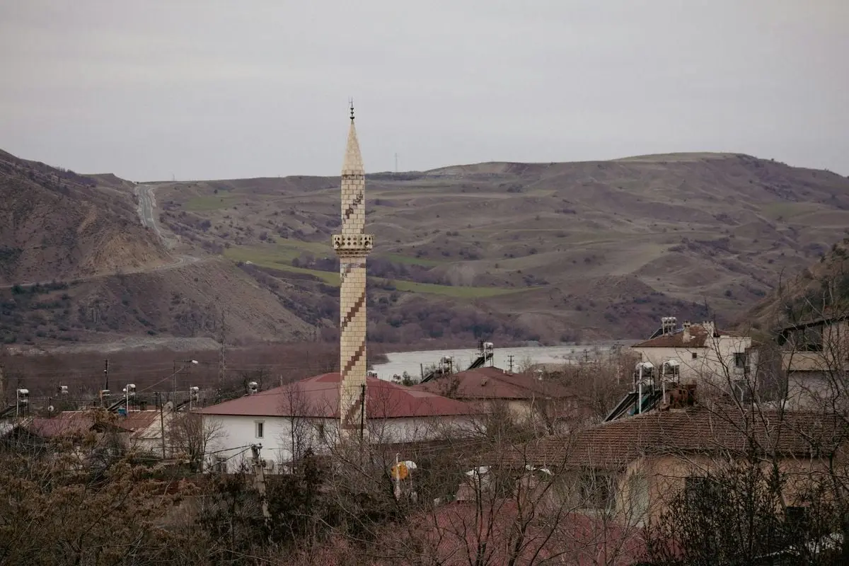 Tranquil scene of a minaret amidst a village and rolling hills in Palu, Türkiye.