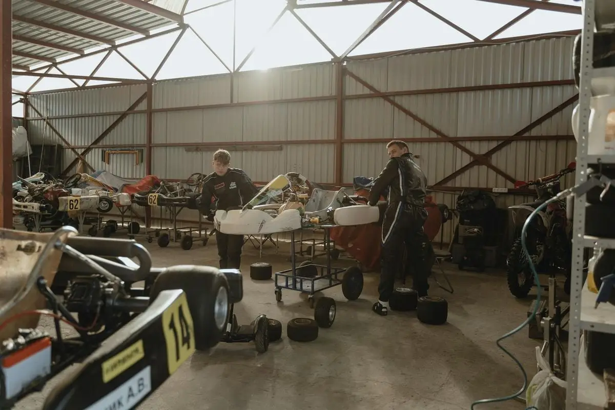 Two mechanics working on go-karts in an indoor workshop with natural lighting.