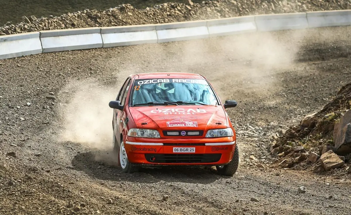 Fiat Palio car speeding through a dusty gravel rally track with skillful maneuvering.
