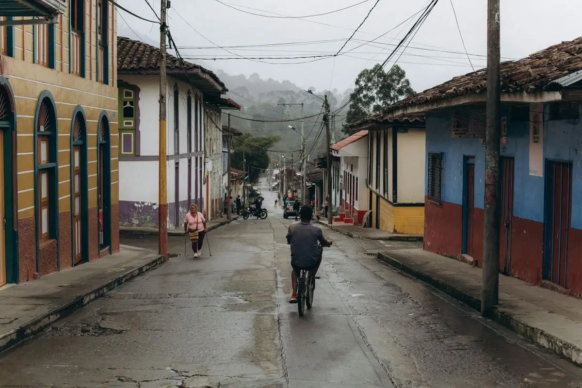 A cyclist rides through a charming town street on a rainy day, capturing the essence of local life.