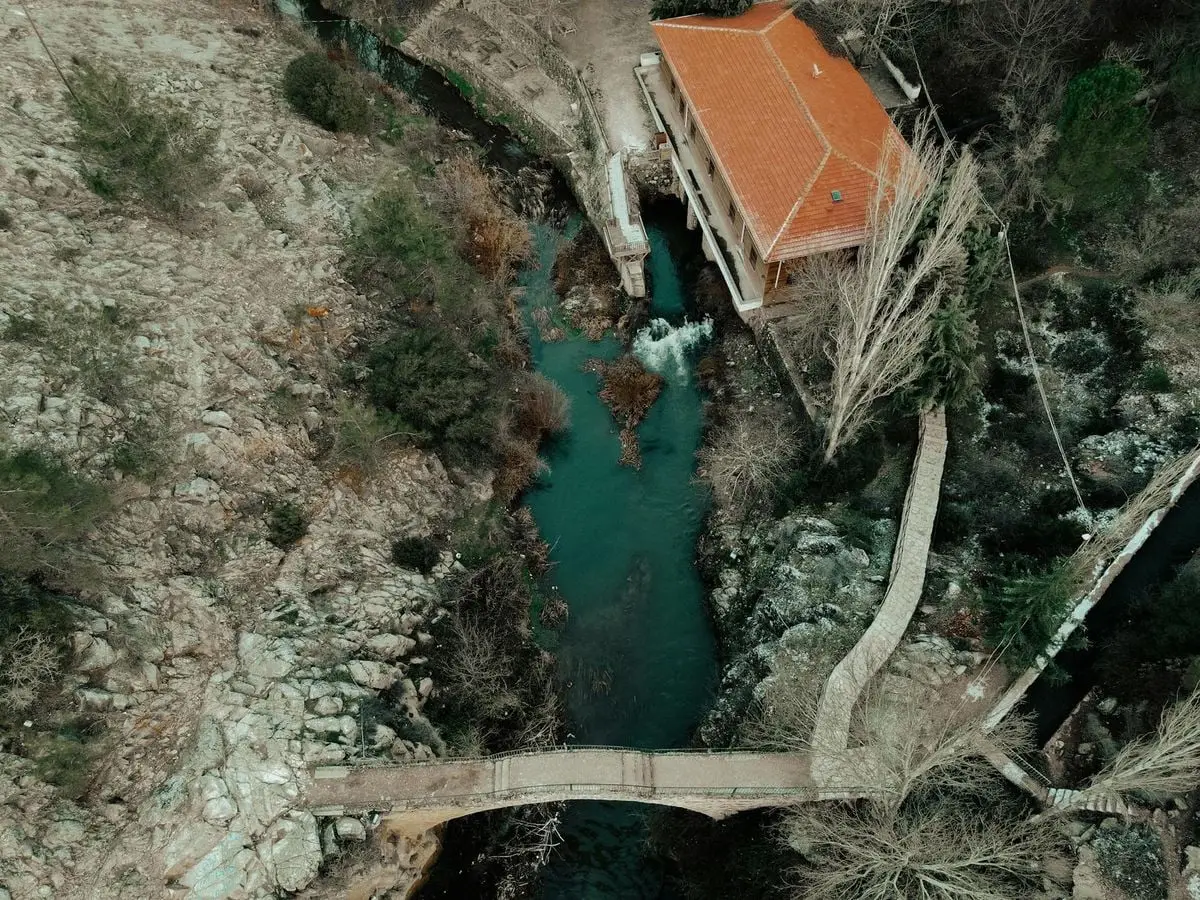 Drone shot of a footbridge over a creek near a house in Uşak, Turkey, showcasing winter scenery.