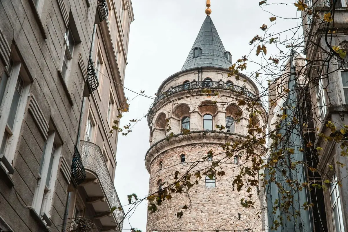 The iconic Galata Tower surrounded by autumn leaves, showcasing historical architecture in Istanbul, Turkey.