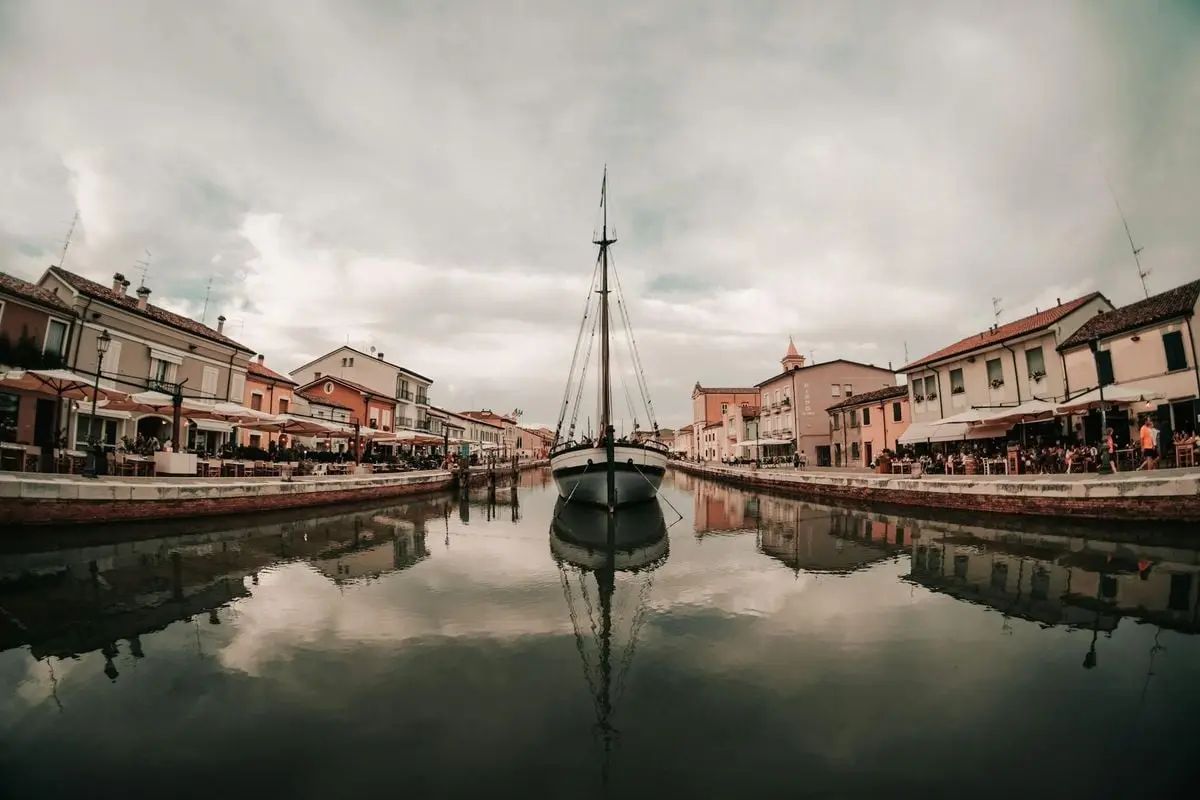 Exterior of small buildings near quiet water of canal with boat under cloudy gloomy sky