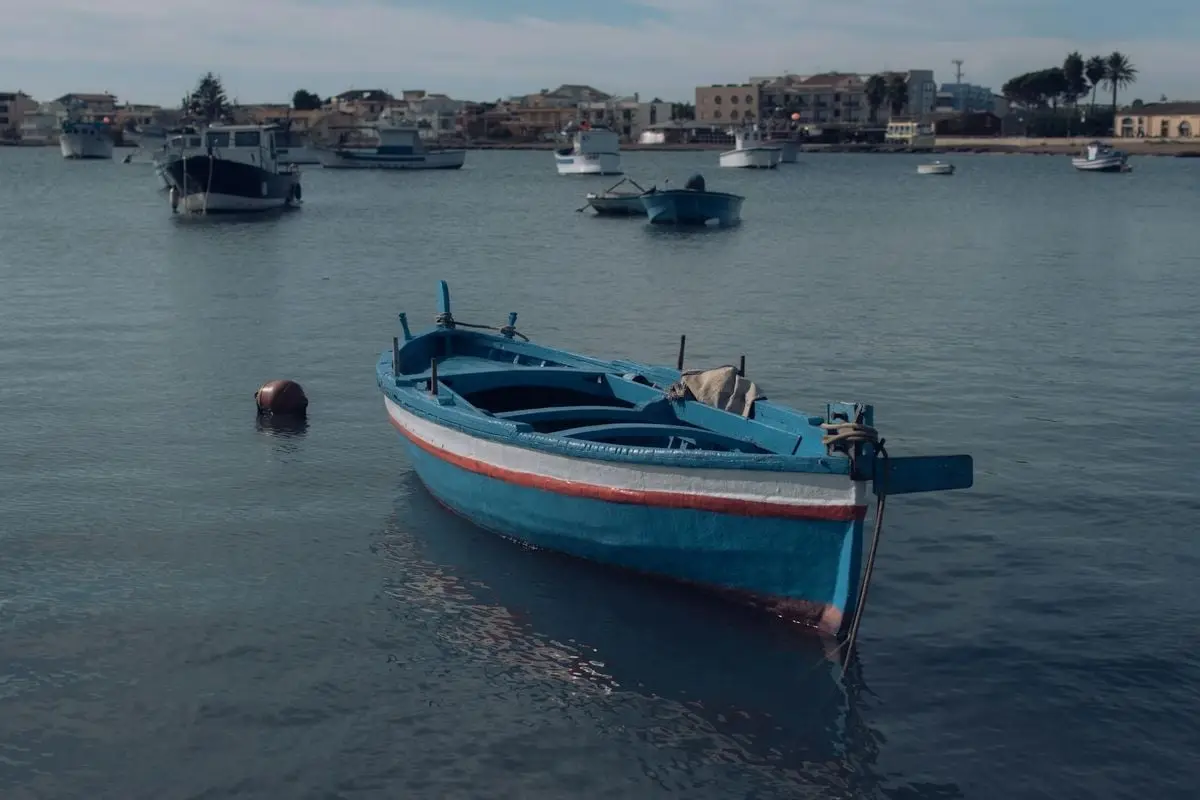Serene view of a blue wooden boat docked in a calm harbor with distant buildings.
