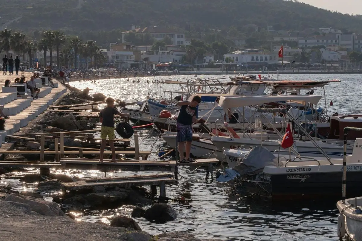 Relaxing summer day at Foça Marina, Türkiye, featuring boats, people, and sparkling water under the sun.