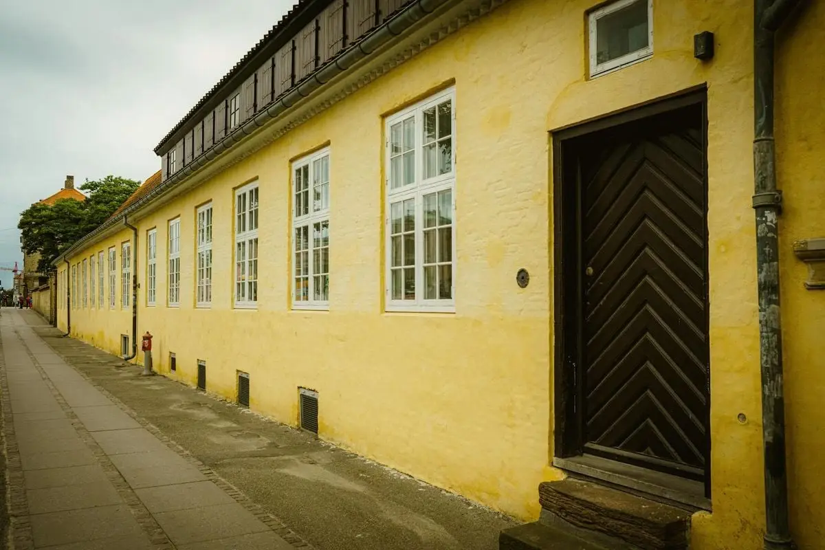 Long yellow facade with windows and a dark wooden door lining a city sidewalk.
