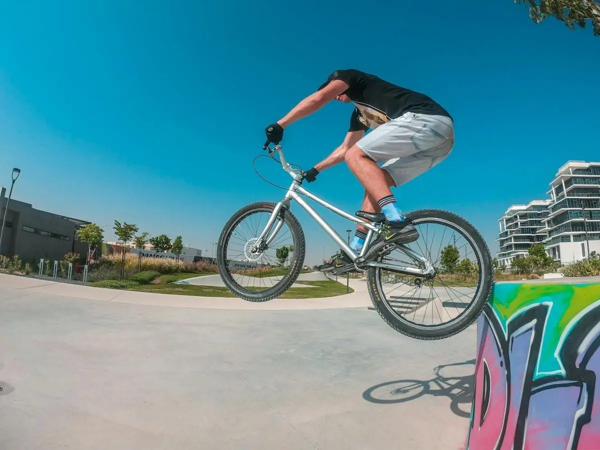 BMX rider performing a jump trick in a sunny urban park in Dubai, showcasing extreme sports action.