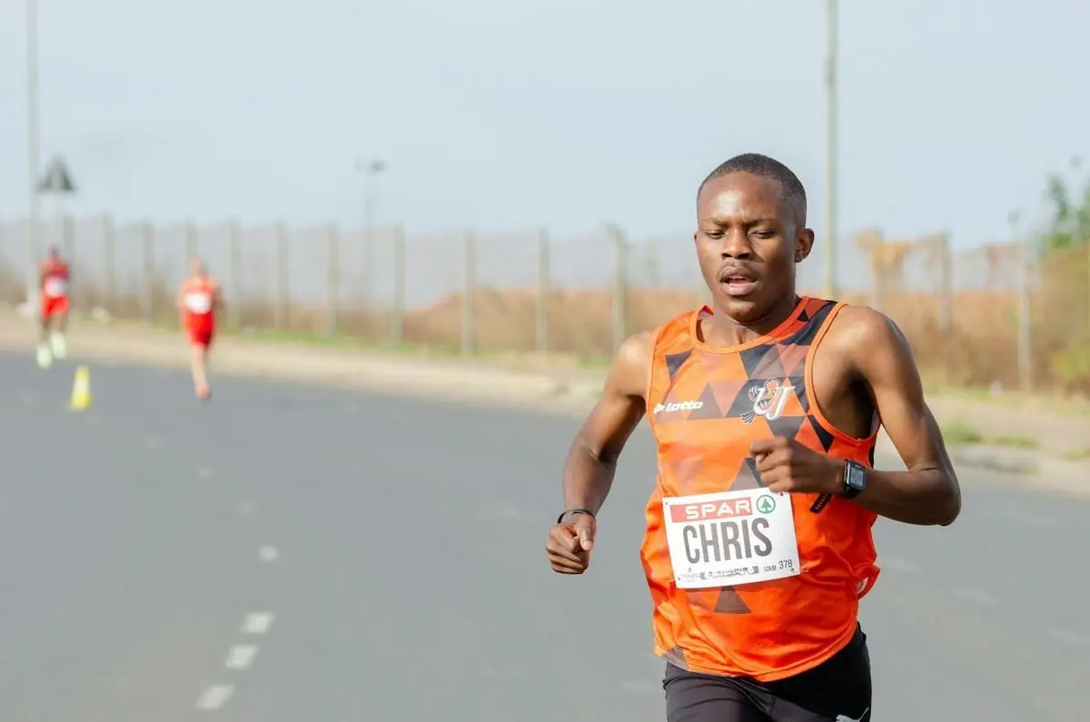 Focused man in an orange tank top running a marathon on a sunny day.