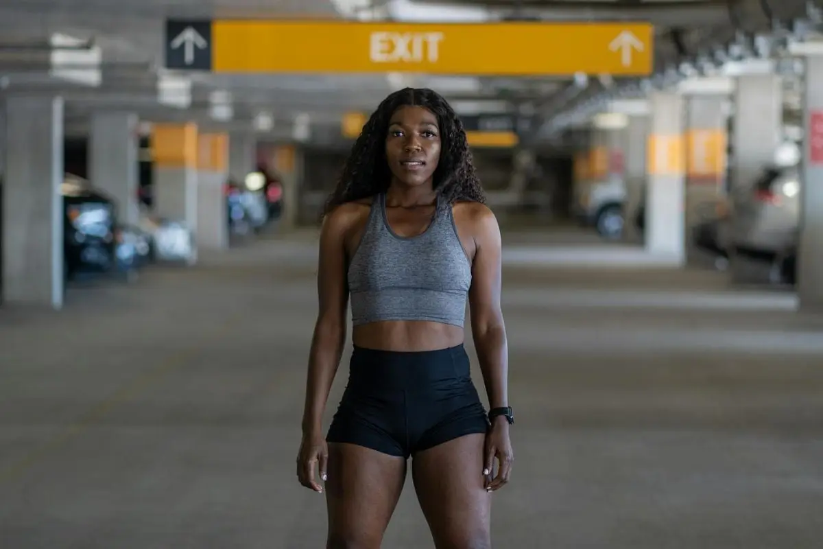 Fit young woman in workout attire standing confidently in a Baltimore parking garage.