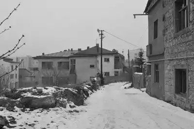 A peaceful winter scene of a snowy street in Kars, Türkiye, framed by traditional stone houses.