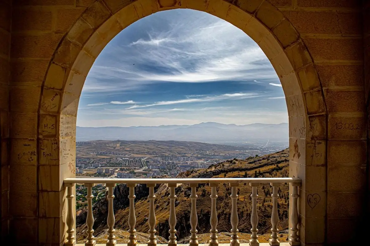 Stunning view of Elazığ cityscape through a historic stone archway, showcasing distant mountains.